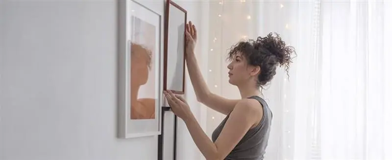 une femme accroche un tableau au mur